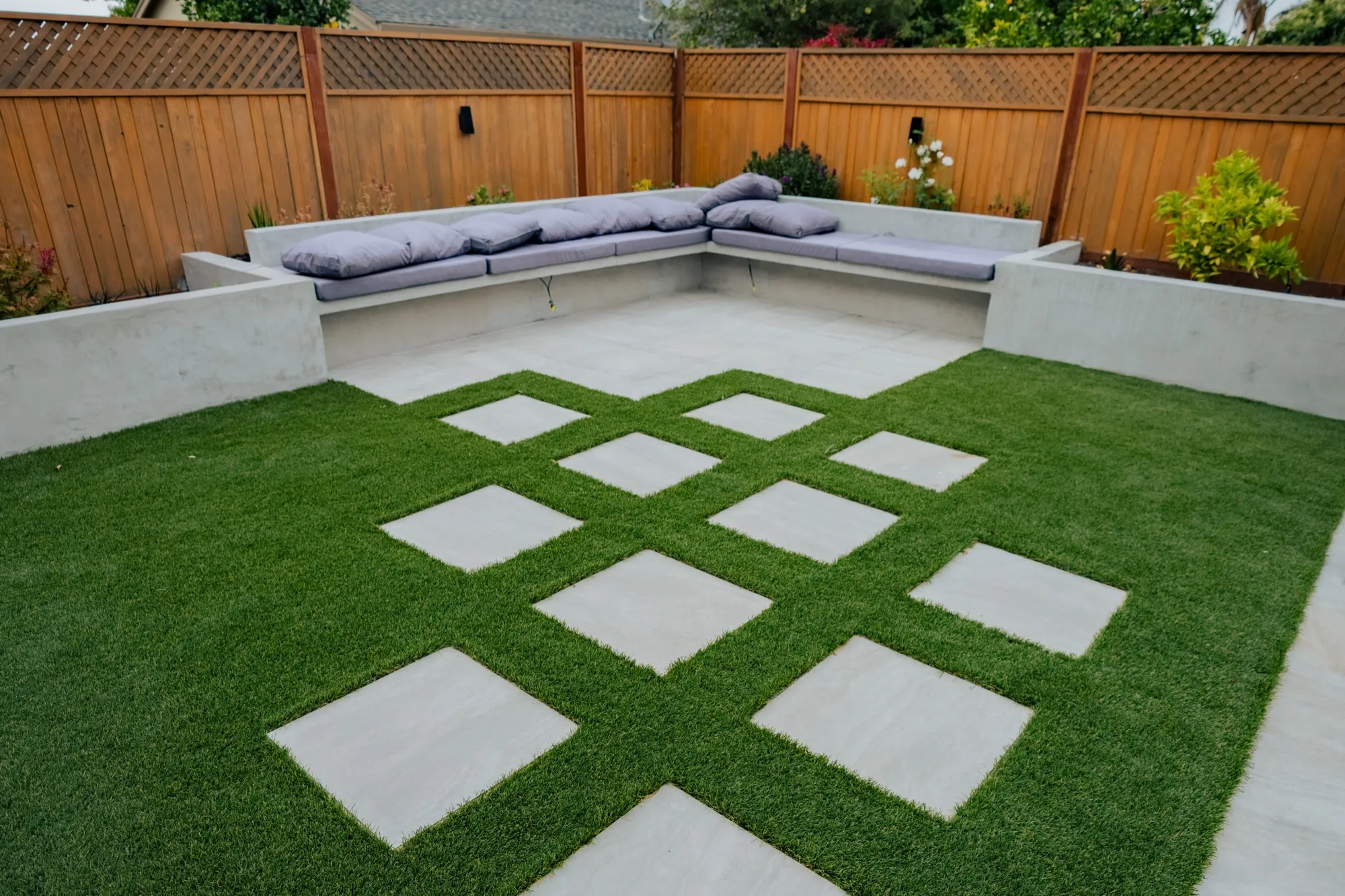 Built-in bench seating with cushions above a checkerboard of pavers and turf